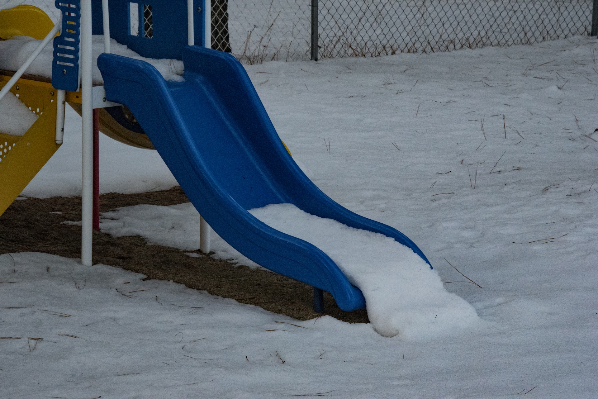 Playground slide in bright blue is covered in white snow