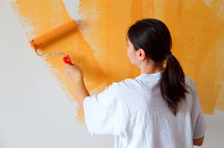 Young woman painting white wall orange