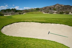 Sand trap lies just to the side of a putting green on a golf course.