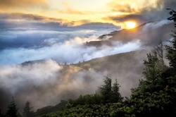 The sun sets as mountains are enveloped in a fog