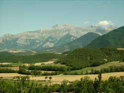 French rocky mountain range on a clear summer day with a view on forests, meadows and a field during harvest.