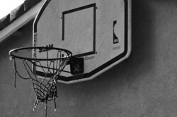 A basketball hoop hooked above a garage with torn net. A hoop that has seen many hours of play