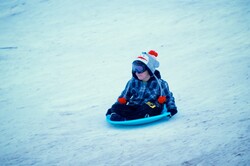 Boy sleds down a hill in winter clothes and a beanie.