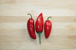 Three red jalapeno peppers lying on a wooden background.