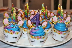 A plate of purple and blue unicorn cupcakes with a number 4 candle.