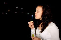 Young woman blowing bubbles on black background 