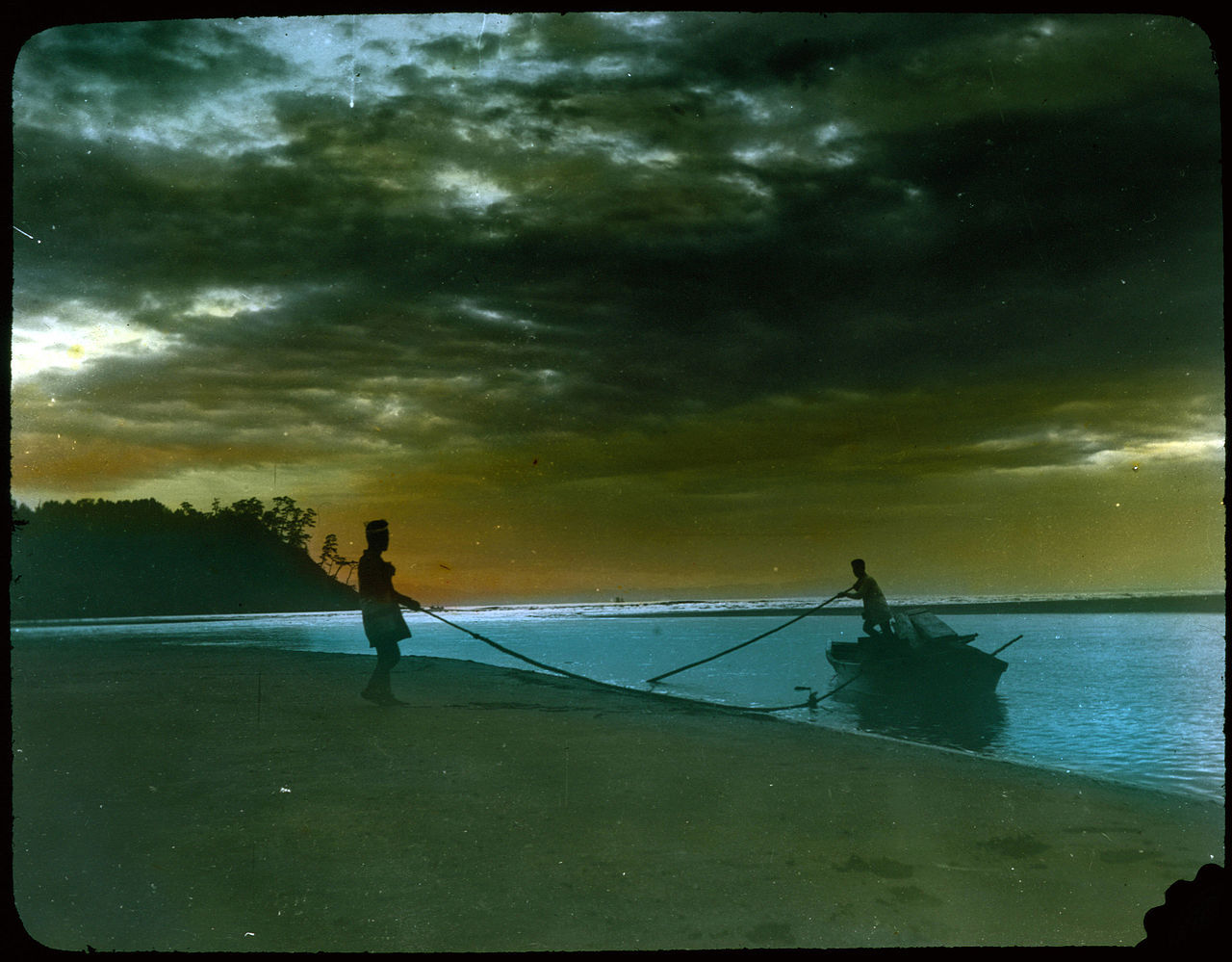 Two men landing boat on beach.