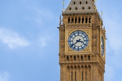 A close-up view of a golden-trimmed Big Ben clock tower in London with a large white clock face set against a clear blue sky.