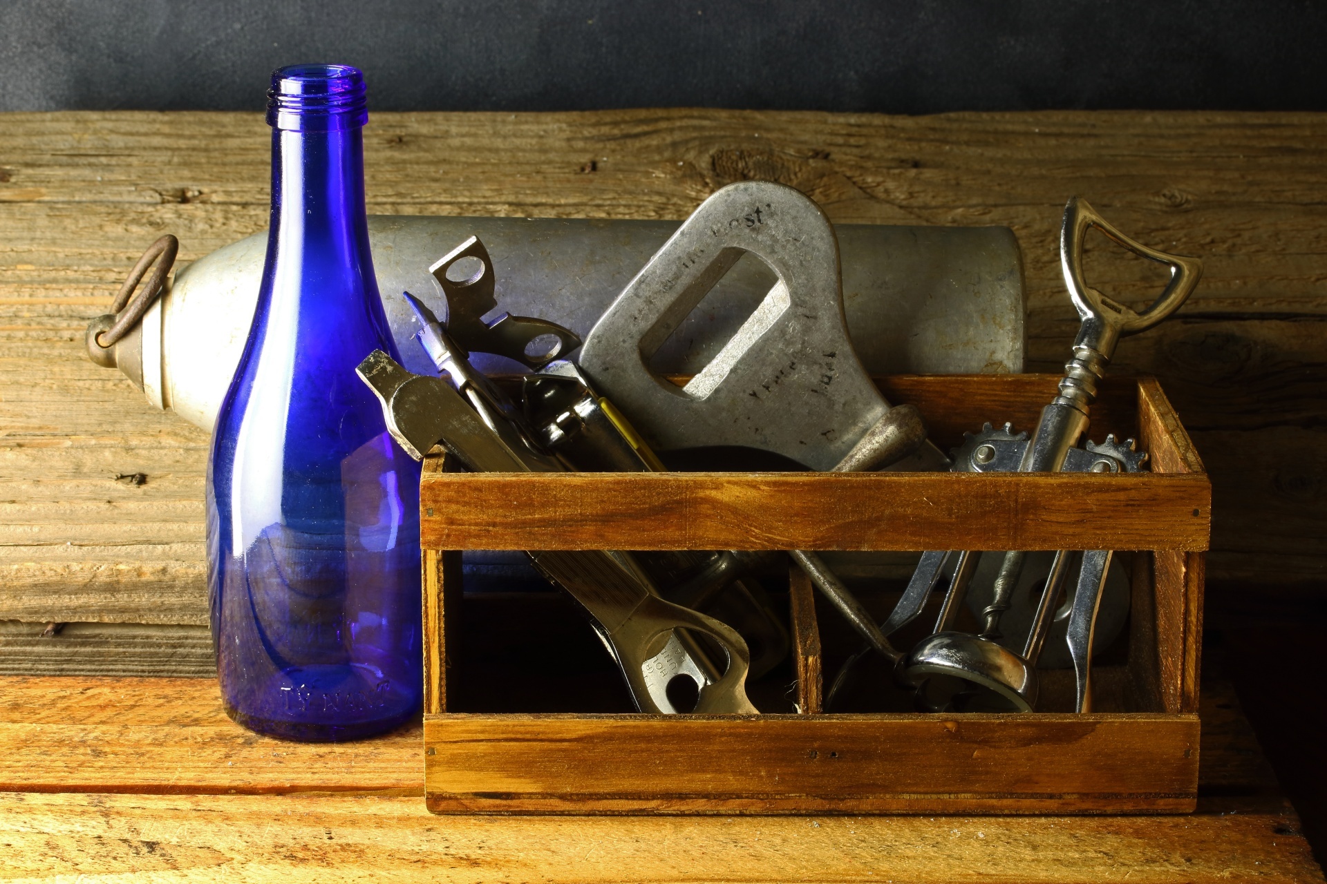 Bottle openers in a small wooden crate with a blue glass bottle and an old metal flask