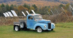 The old and the new - old rusty blue pick-up truck parked in front of a field of solar panels. Fall foliage in the mountains