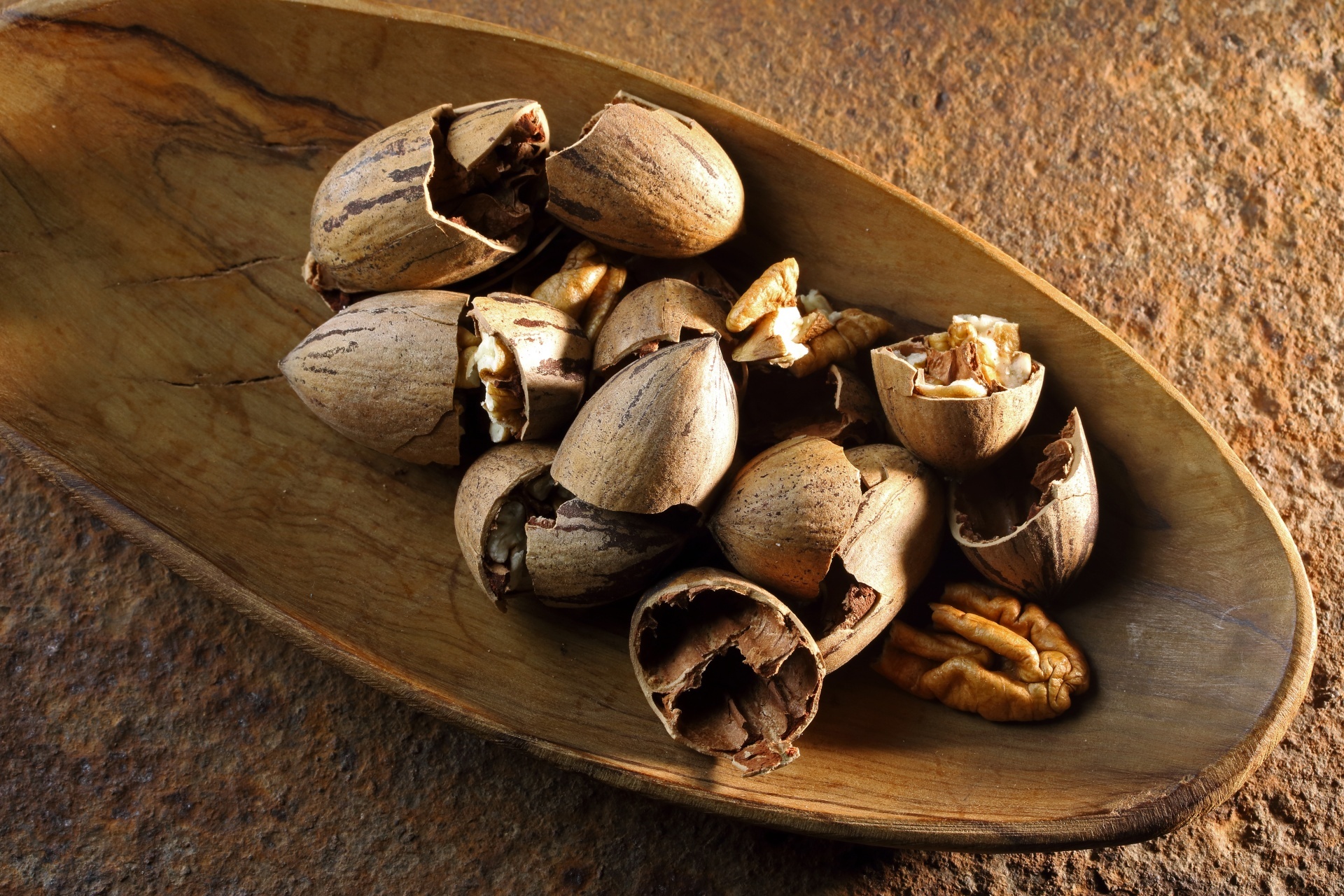 Pecan nuts broken open with shells in a wooden bowl