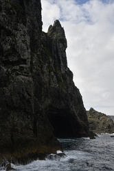 Rugged cliffs and dramatic rock formations in the Bay of Islands, New Zealand, under a cloudy blue sky