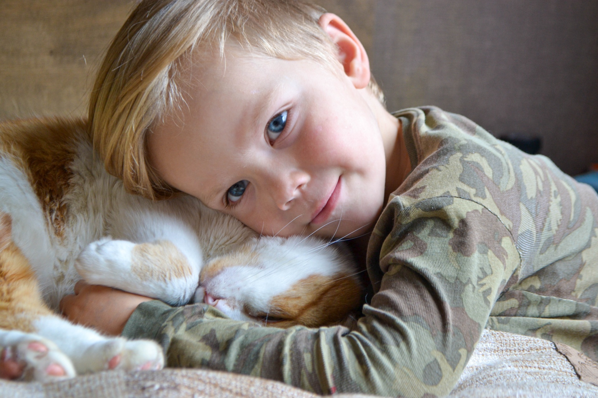 Portrait of happy adorable child aged four years old on the bed in his room whit sleeping red cat. Thoughtful look. High quality photo