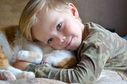 Portrait of happy adorable child aged four years old on the bed in his room whit sleeping red cat. Thoughtful look. High quality photo