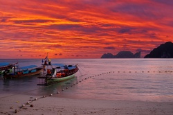 Two boats moored on a beach with a dramatic sunset backdrop