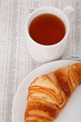 Breakfast With Market Data: Cup of tea and a croissant on a plate on newspaper with market data