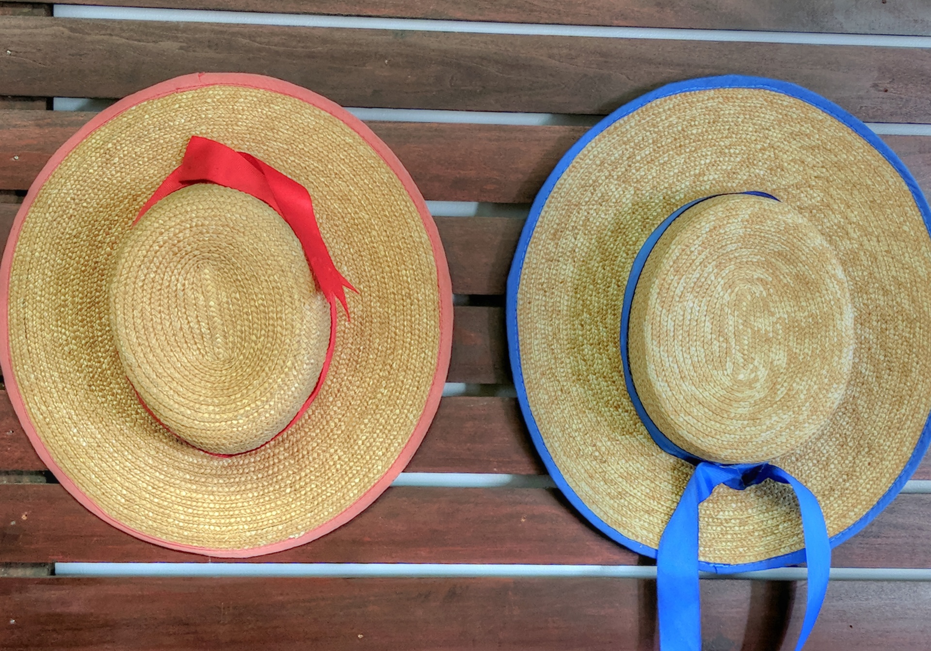 Two straw hats with ribbon hanging on a board one with blue ribbon and other with Red ribbon