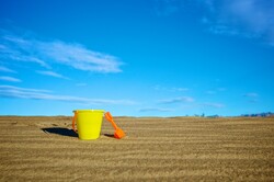 Yellow plastic sand bucket and orange shovel on the side of a sand dune.