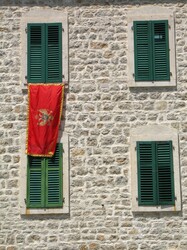 Stone wall, green shutters and flag of Montenegro