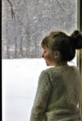 Little girl is standing in a window, watching the snow outside