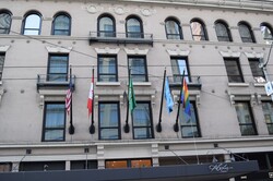 Five flags in front of a building, including the US flag, Canadian flag, and gay pride flag.