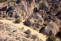 Horse and rider wander a dust dirt path through the desert of southern California.