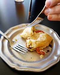 Image of a savory croissant pastry with mozzarell and tomatoes served on a decorative pewter plate being enjoyed mid-meal