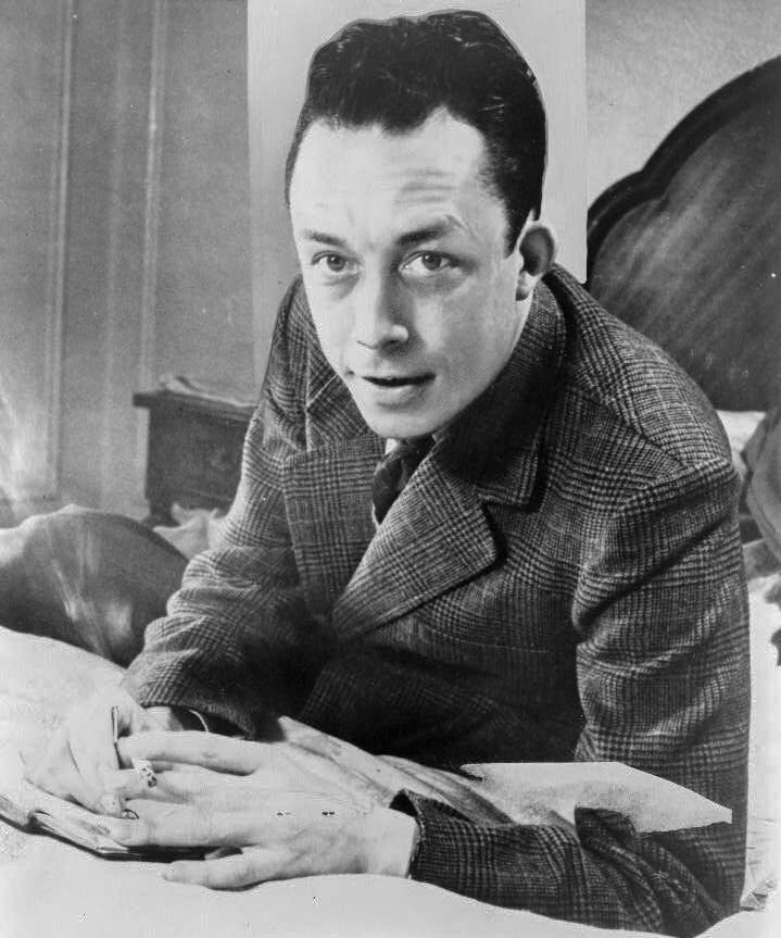 Albert Camus, Nobel prize winner, half-length portrait, seated at desk, facing left, smoking cigarette