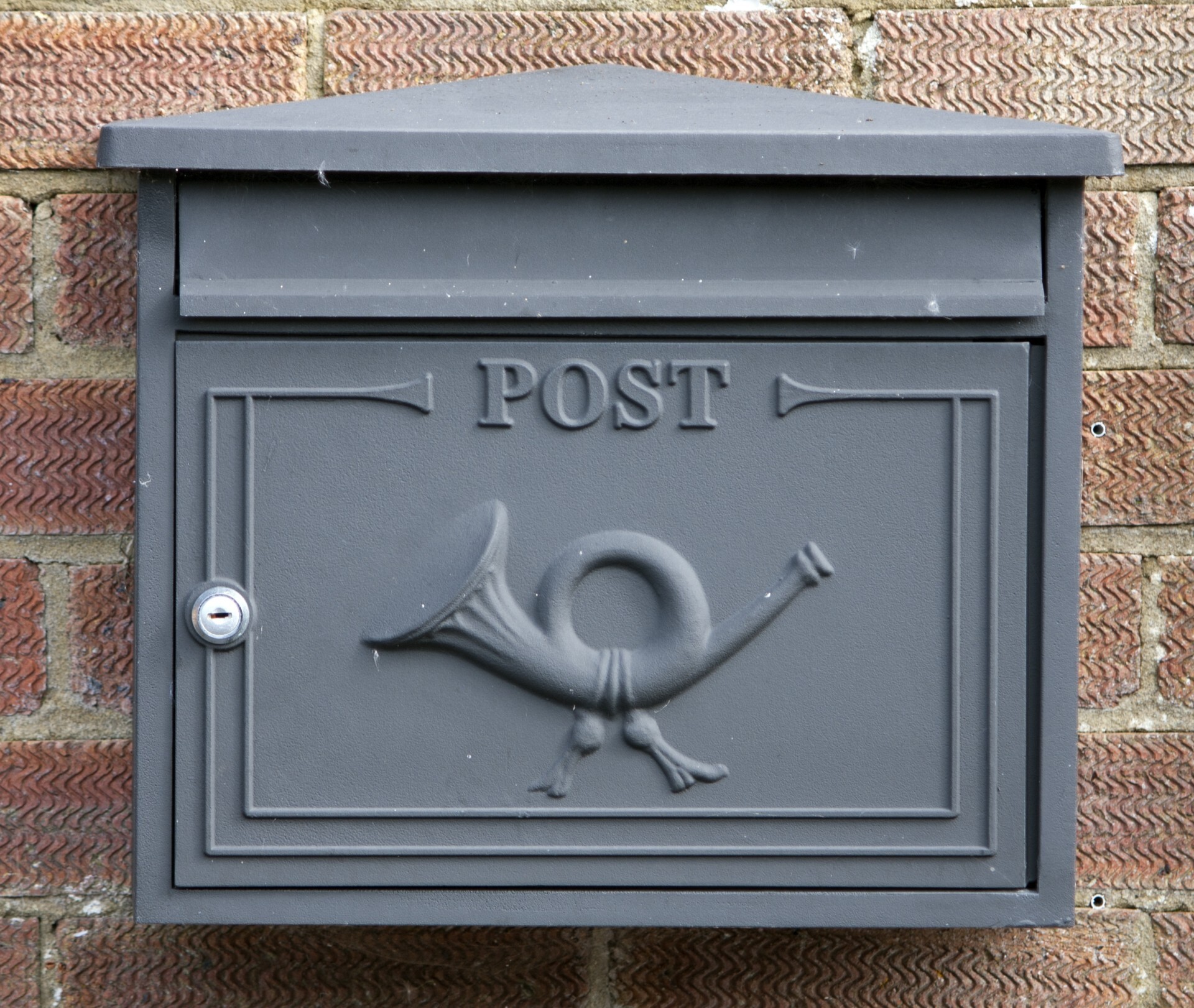 Grey steel post box mounted on brick wall