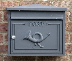 Grey steel post box mounted on brick wall