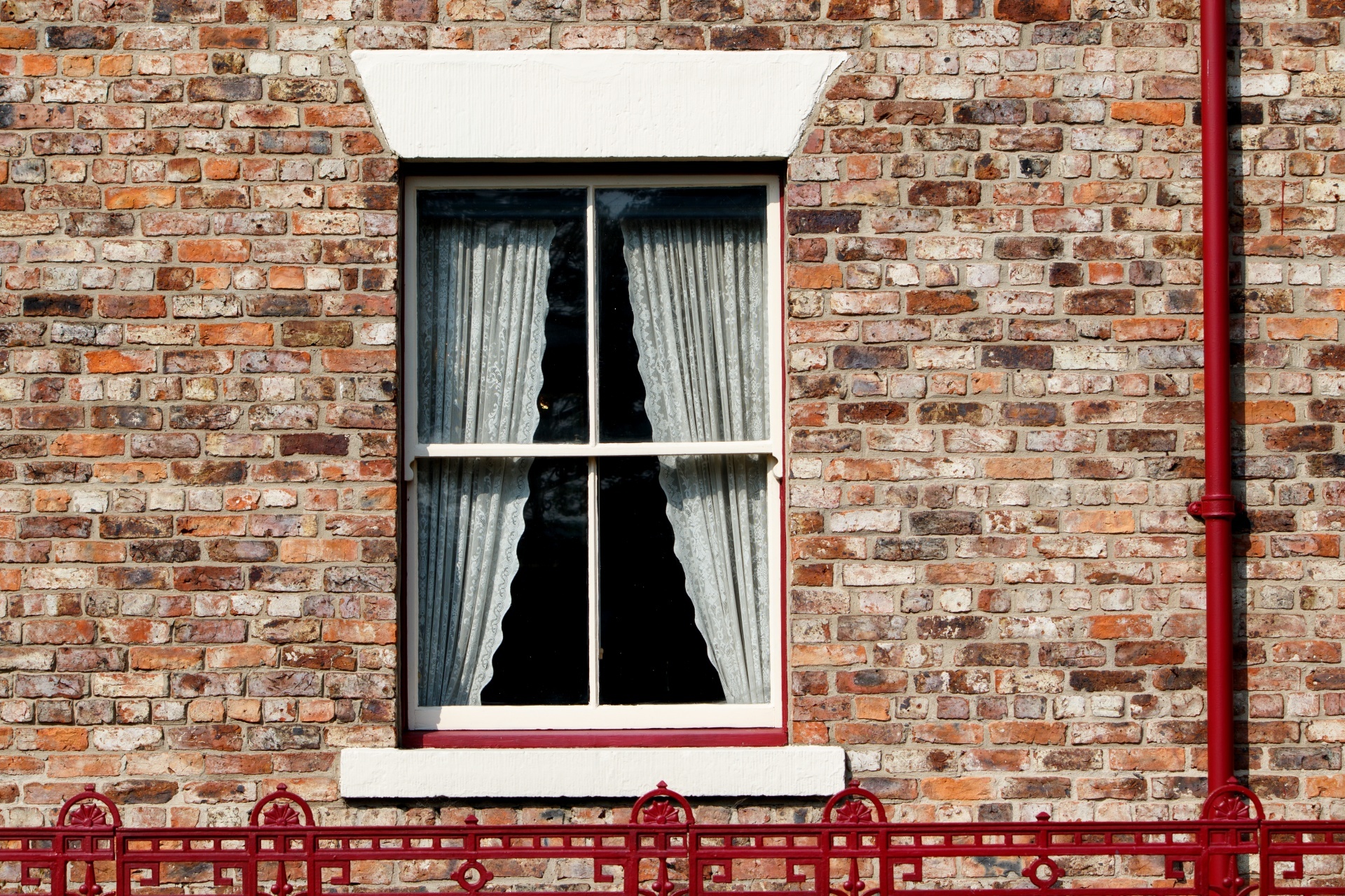 Vintage victorian window with lace net curtains and red brick and metal railing fence