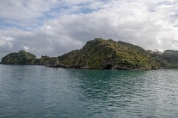 Islands with rich vegetation and a prominent sea cave along the coast of the Bay of Islands, New Zealand, under cloudy skies
