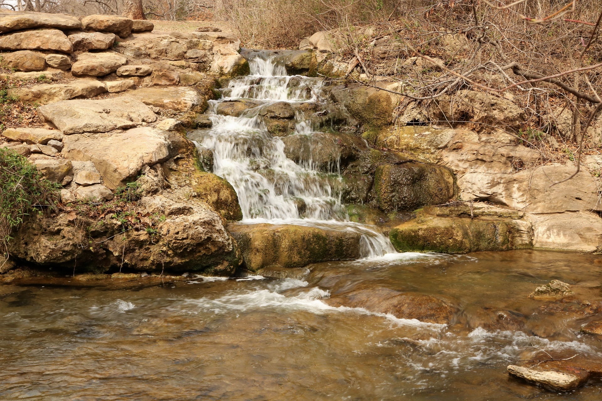 A small waterfall cascading over rocks and into a slow running stream in winter.