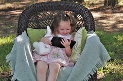 A cute little girl, sitting outside in a wicker chair, watching videos on a tablet.